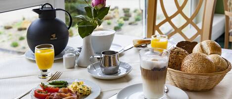 Un desayuno con una mesa dispuesta para dos personas, incluyendo platos de comida, una jarrón, una taza y una cesta de pan.