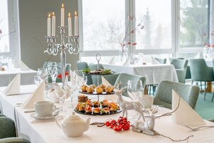 Una mesa de comedor dispuesta con una fuente de postres escalonada, una tetera blanca y velas decorativas.