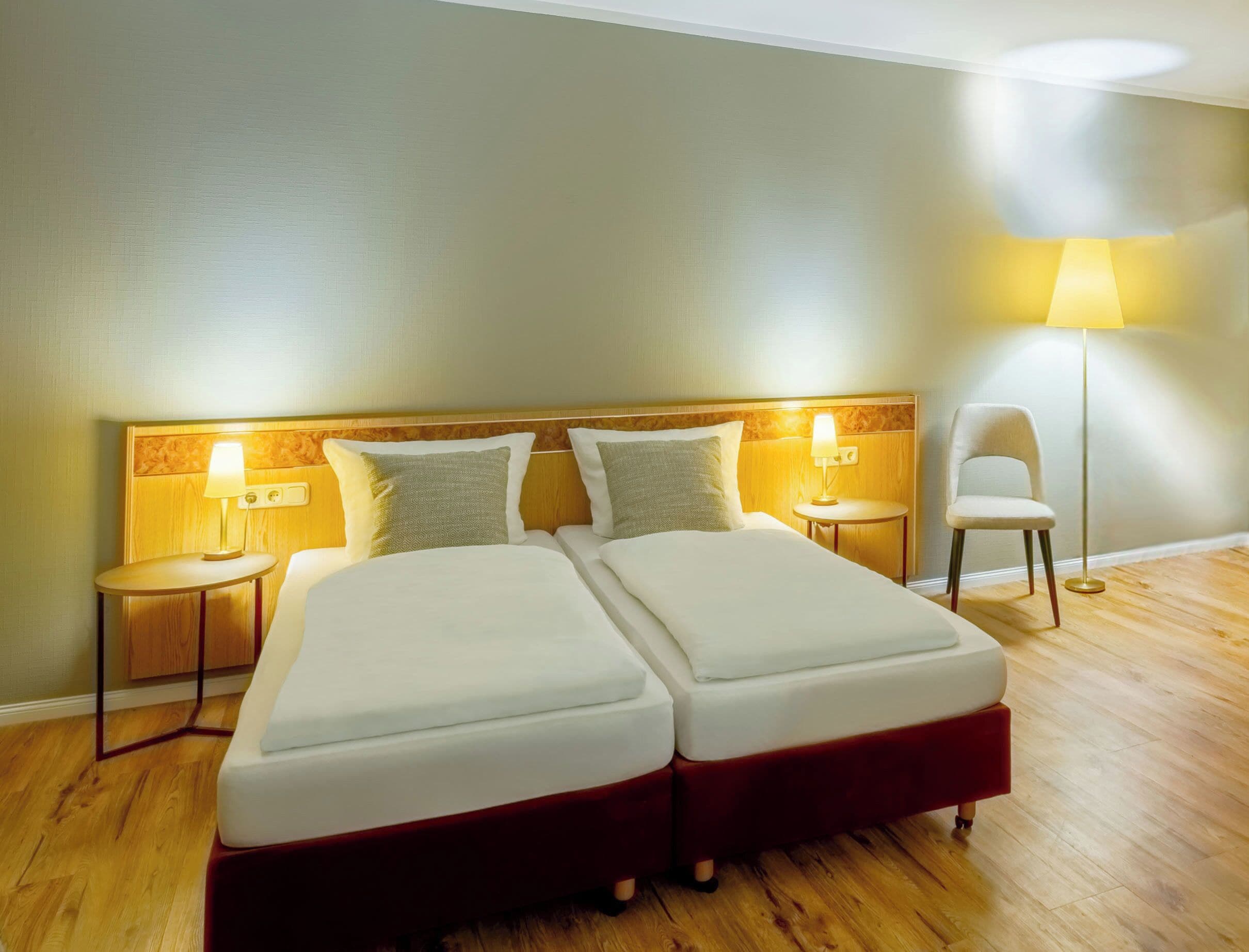 Una habitación de hotel con dos camas, una mesita de noche, una lámpara y una silla.
