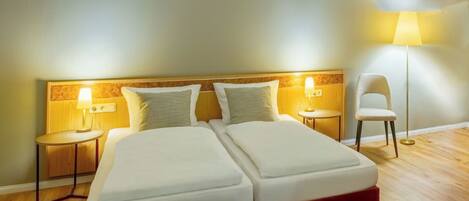 Una habitación de hotel con dos camas, una mesita de noche, una lámpara y una silla.