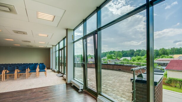 A spacious room with large windows, a wooden floor, and rows of blue chairs. - Hotel Tigra (Priekuli)