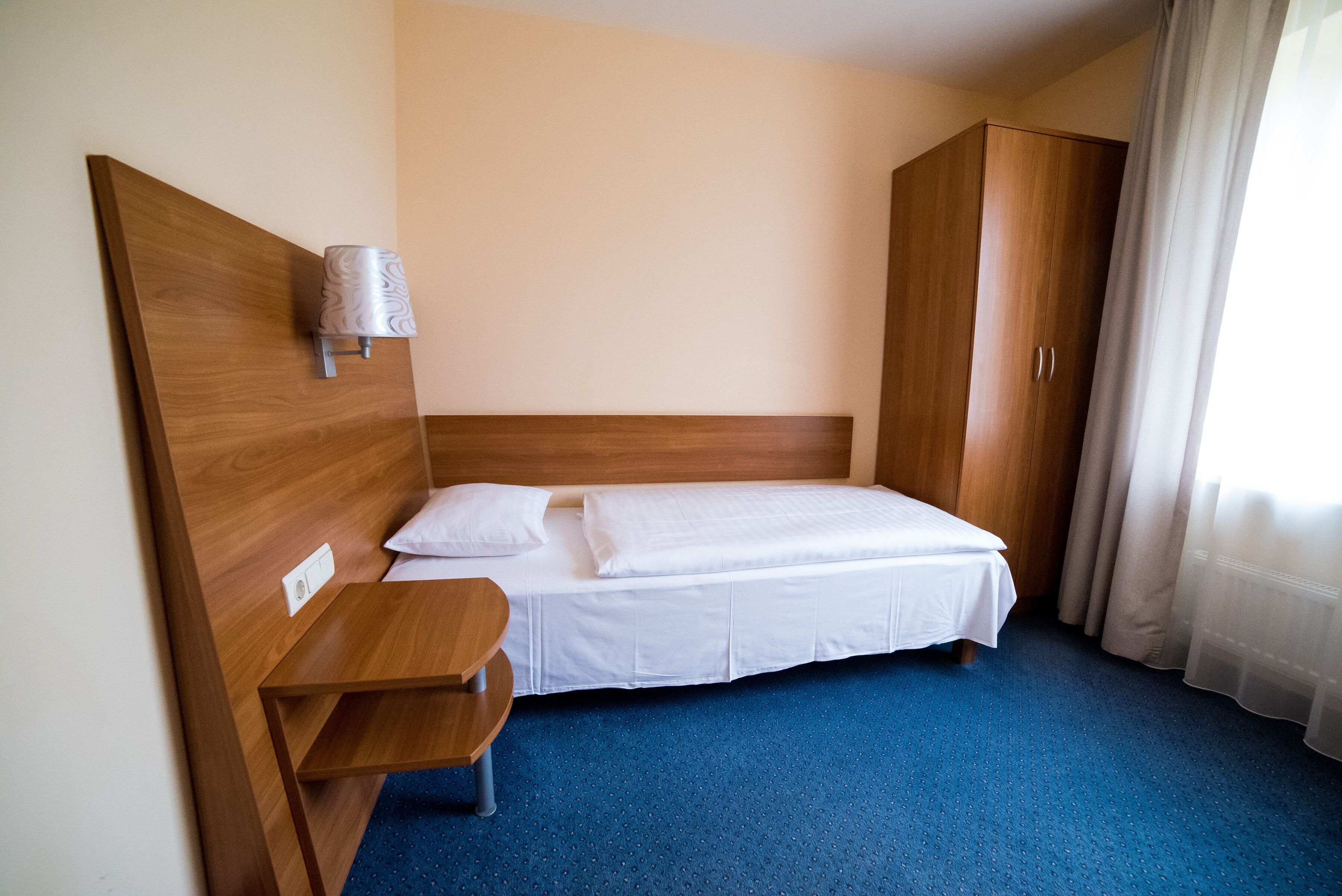 Una habitación de hotel con cabecera de madera, una cama individual con ropa blanca, una mesita de noche de madera y un armario.