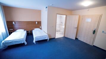 Une chambre d’hôtel avec deux lits simples, une tête de lit en bois, une moquette bleue et une porte donnant sur une salle de bain.