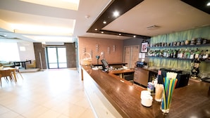 A hotel lobby with a reception desk, a bar area with shelves of bottles, and a seating area with chairs and a table. - Hotel Tigra (Priekuli)
