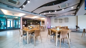 A spacious dining area with wooden tables and chairs, a bar in the background, and a modern ceiling design. - Hotel Tigra (Priekuli)