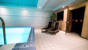 A swimming pool with tiled walls, two lounge chairs, a potted plant, and a door leading to a dark room. - Hotel Tigra (Priekuli)
