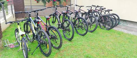 Varias bicicletas aparcadas en un césped frente a un edificio con pared de ladrillo y una ventana.