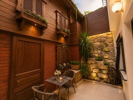 Un espacio de estar al aire libre acogedor, con pared de piedra, contraventanas de madera y una mesa con sillas.