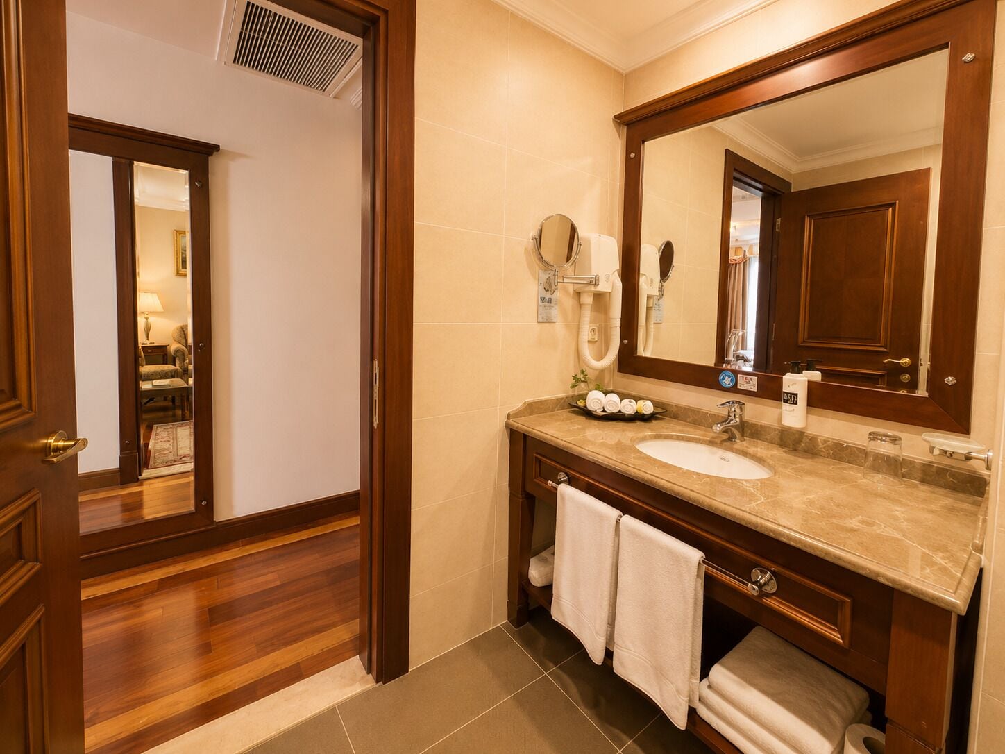Un baño de hotel con un tocador de madera, un espejo grande, un lavabo y un perchero para toallas.