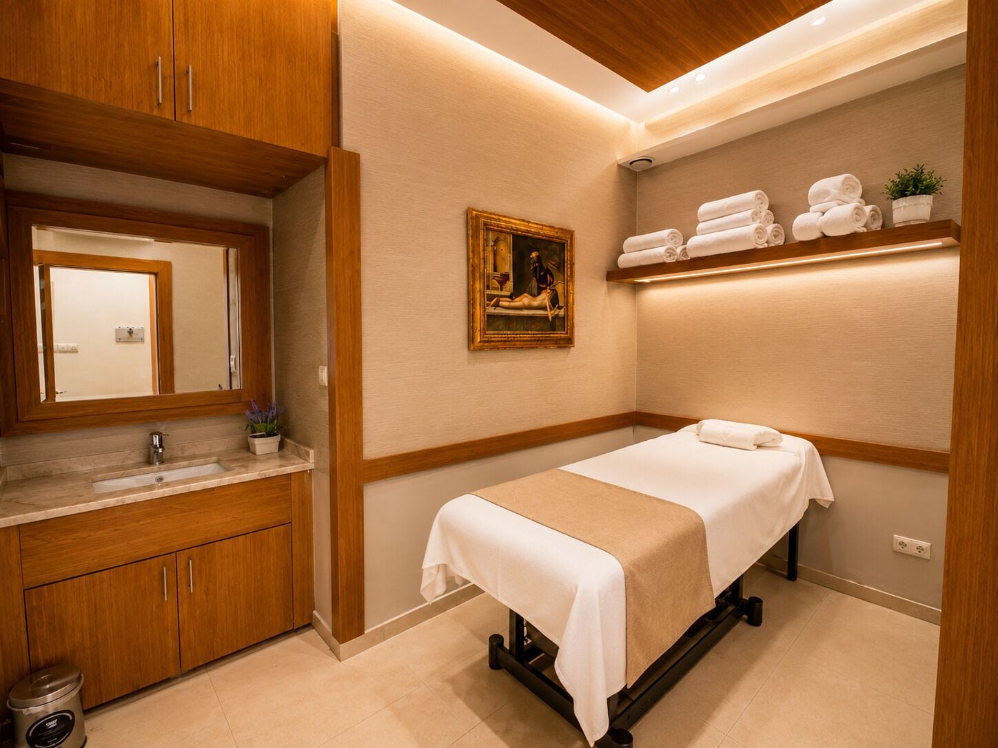 Una habitación con un armario de madera, un lavamanos, un cuadro, una estantería con toallas y una cama.