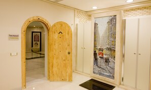 A hallway with a wooden door labeled "Turkish Bath," a tiled wall, and a painting of a snowy street scene. - GLK PREMIER Regency Suites & Spa - Special Class (Istanbul)