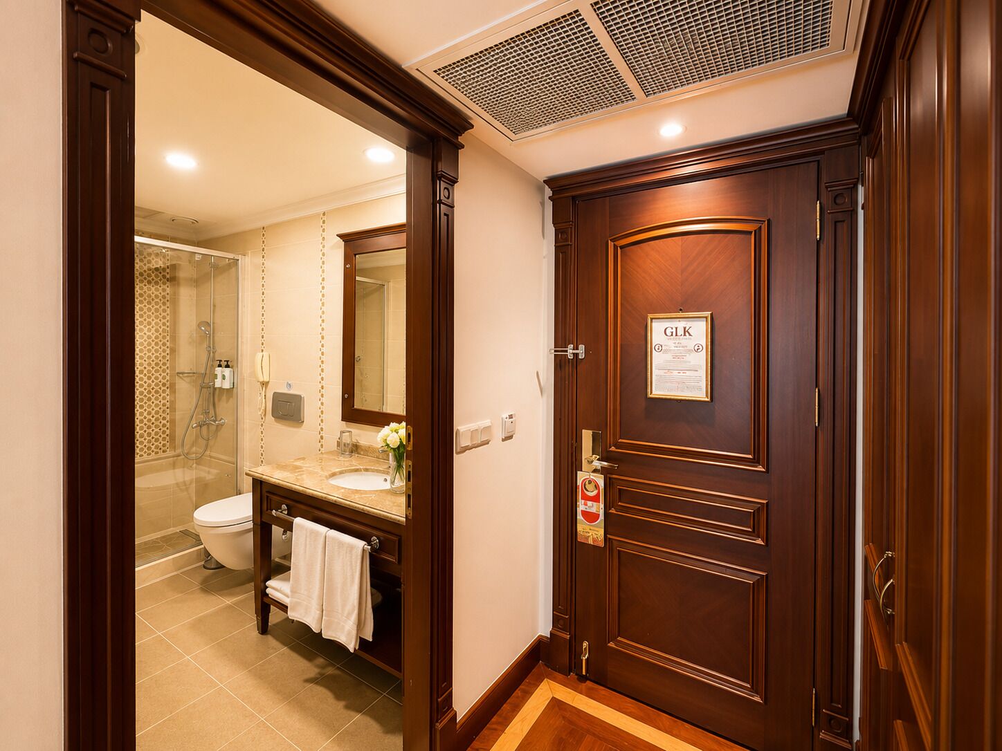 A hotel bathroom with a wooden vanity, a mirror, a toilet, and a shower area.