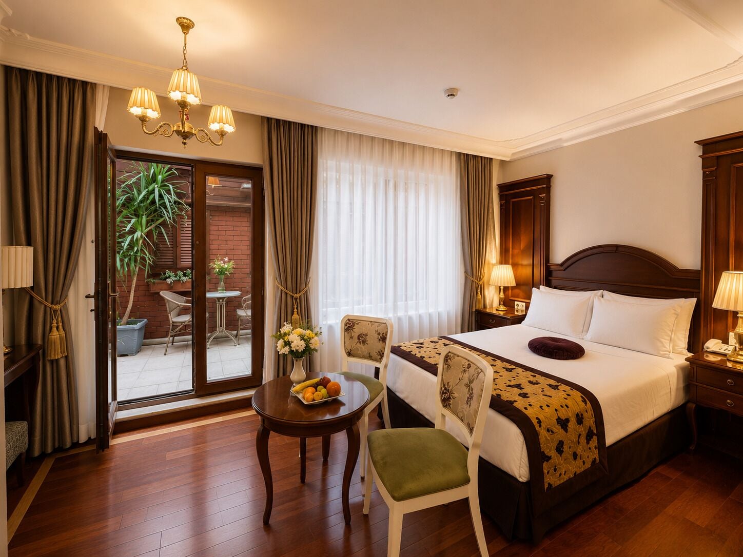 A hotel room with a bed, bedside tables, a chair, a small table with fruit, and a view of the outside.