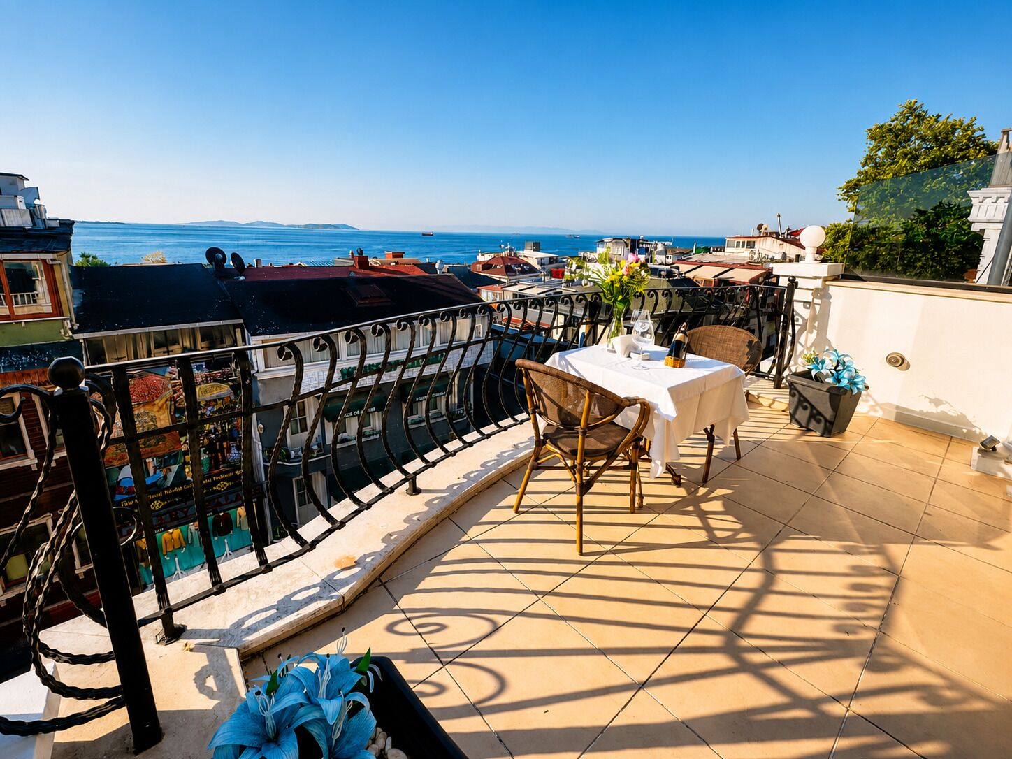 A terrace with a table and chairs, overlooking a coastal area with boats and buildings.