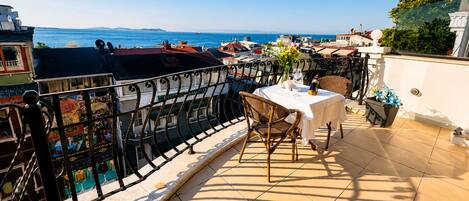 A terrace with a table and chairs, overlooking a coastal area with boats and buildings.