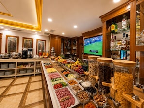 A buffet area with a variety of food options and a television displaying a sports event. - GLK PREMIER Regency Suites & Spa - Special Class (Istanbul)