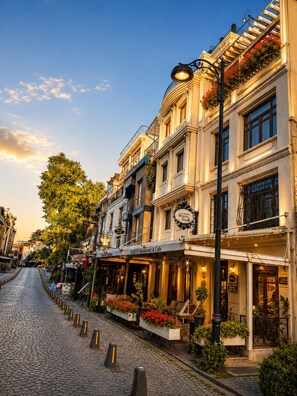 Una calle adoquinada flanqueada por edificios históricos, un restaurante jardín y un cartel de hotel visible.