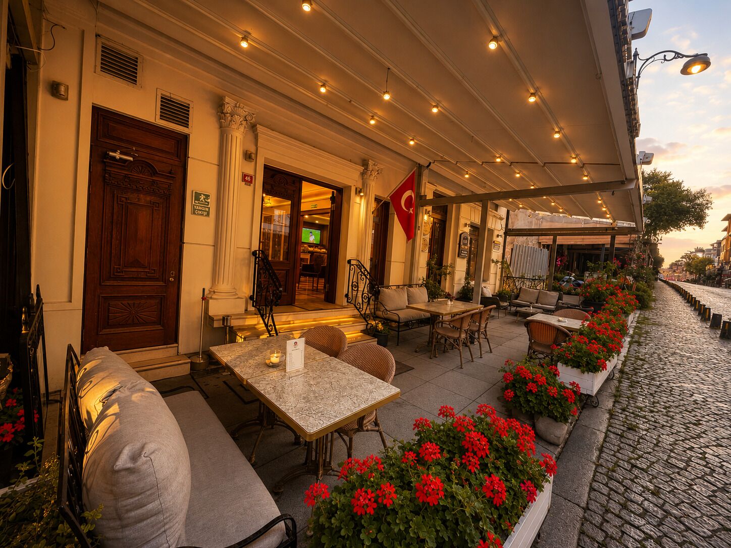 An outdoor café area with tables and chairs, a Turkish flag, and a cobblestone street.