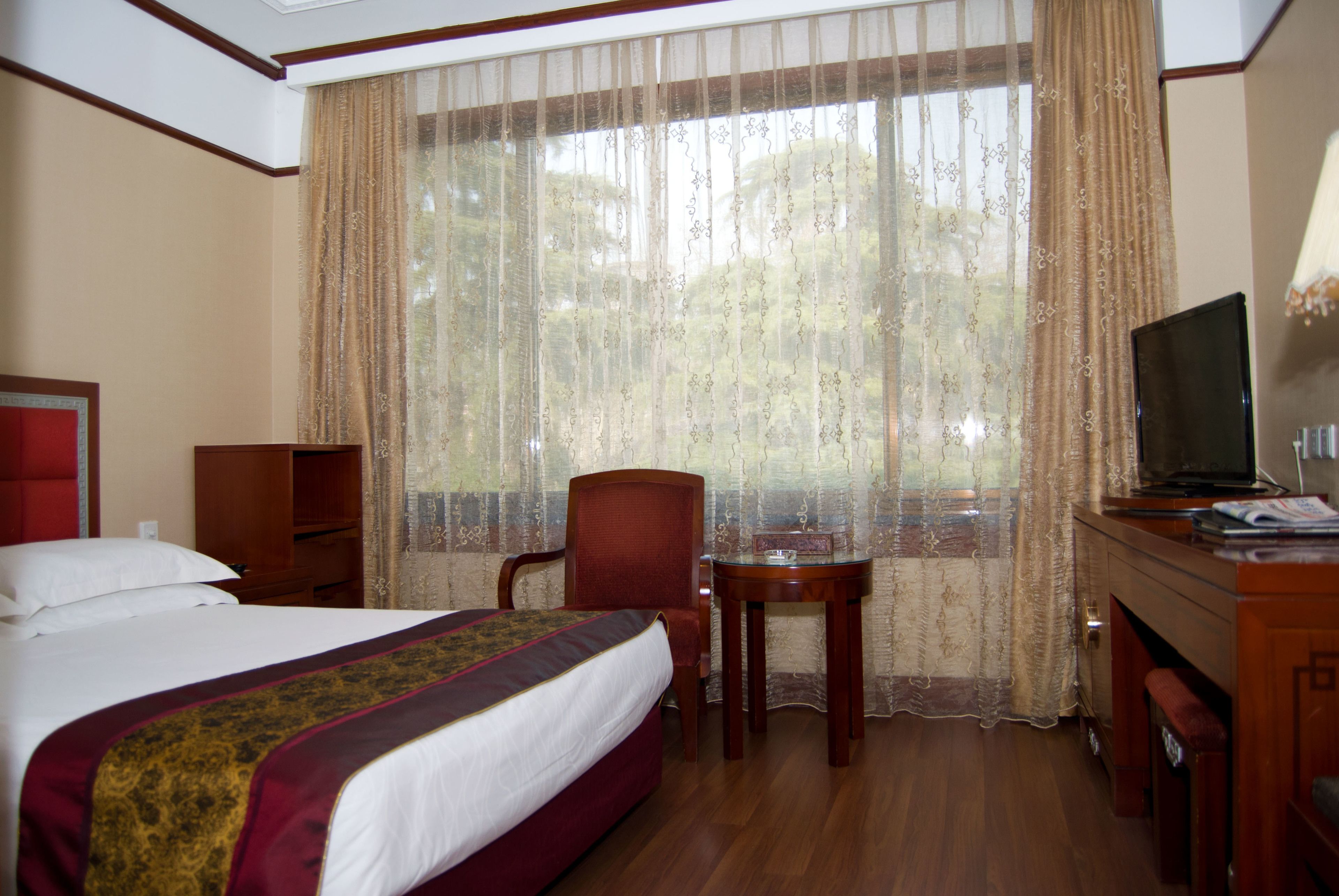 A hotel room with a bed, a desk, a chair, a television, and a window with curtains.