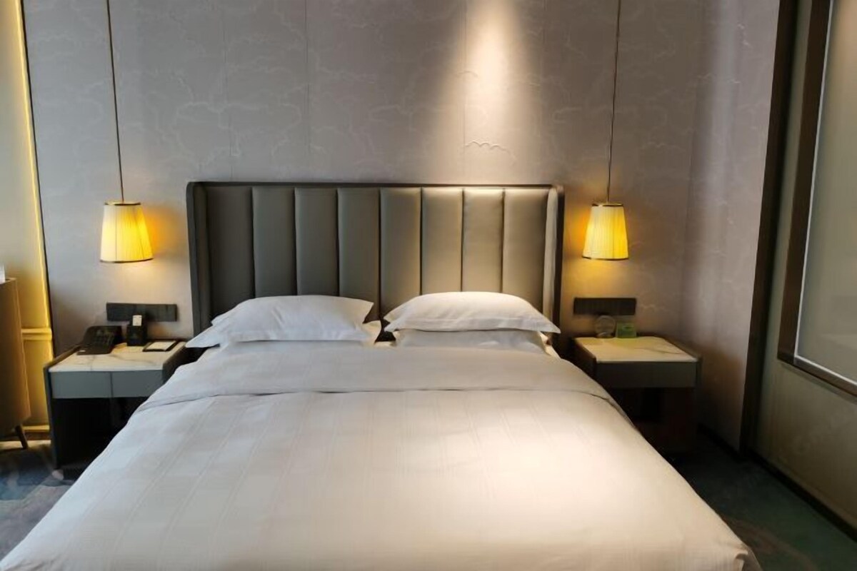 A hotel room with a large bed, two bedside tables, and two lamps.