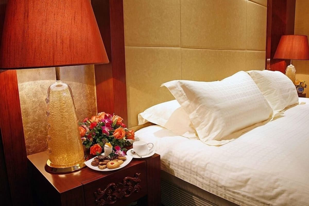 Une chambre d’hôtel avec un lit, une table de chevet avec une lampe, un vase de fleurs et une assiette de biscuits.