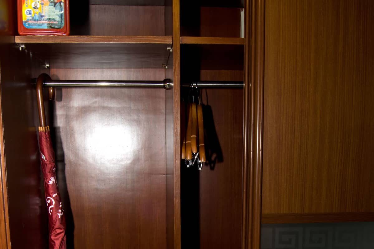 Une armoire en bois avec un porte-chaussures en bas, un parapluie suspendu et une petite étagère sur laquelle se trouve une boîte.