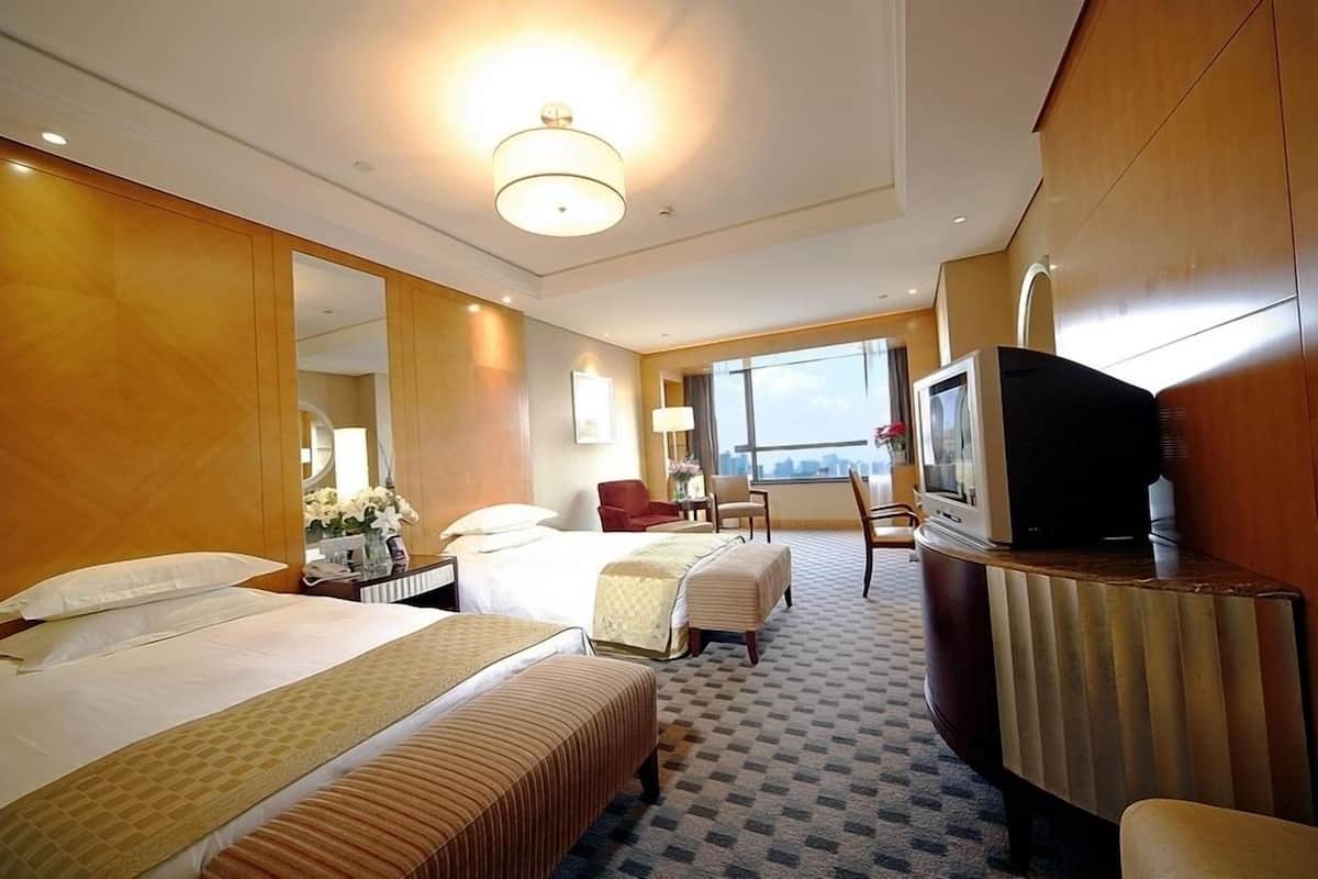 Une chambre d’hôtel avec deux lits, une télévision, un bureau et une grande fenêtre.