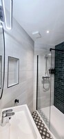 Ein modernes Badezimmer mit einer weißen Badewanne, einer in Glas abgeschirmten Dusche und einem schwarz-weißen Bodenbelag.