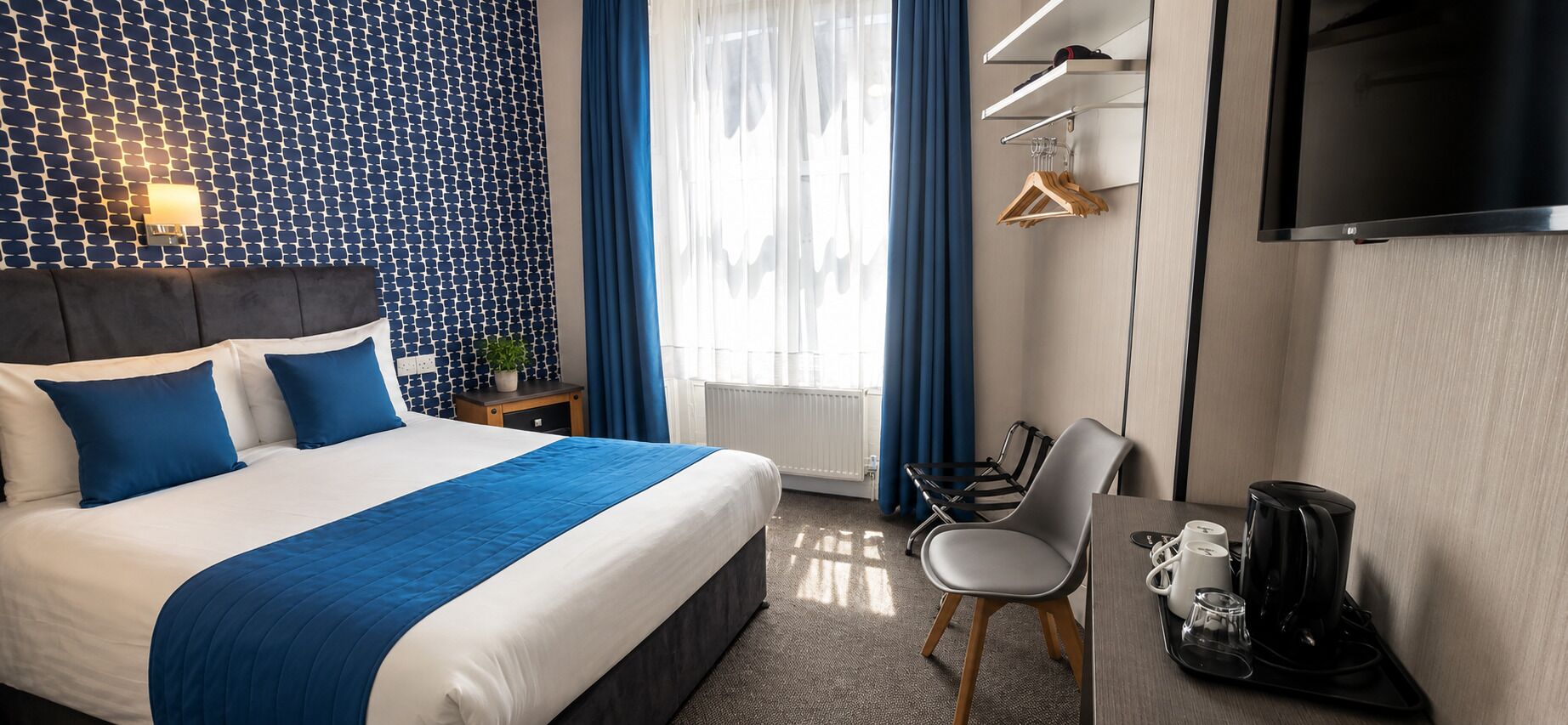 Una habitación de hotel con una cama, un escritorio con una silla, una cafetera y un televisor.