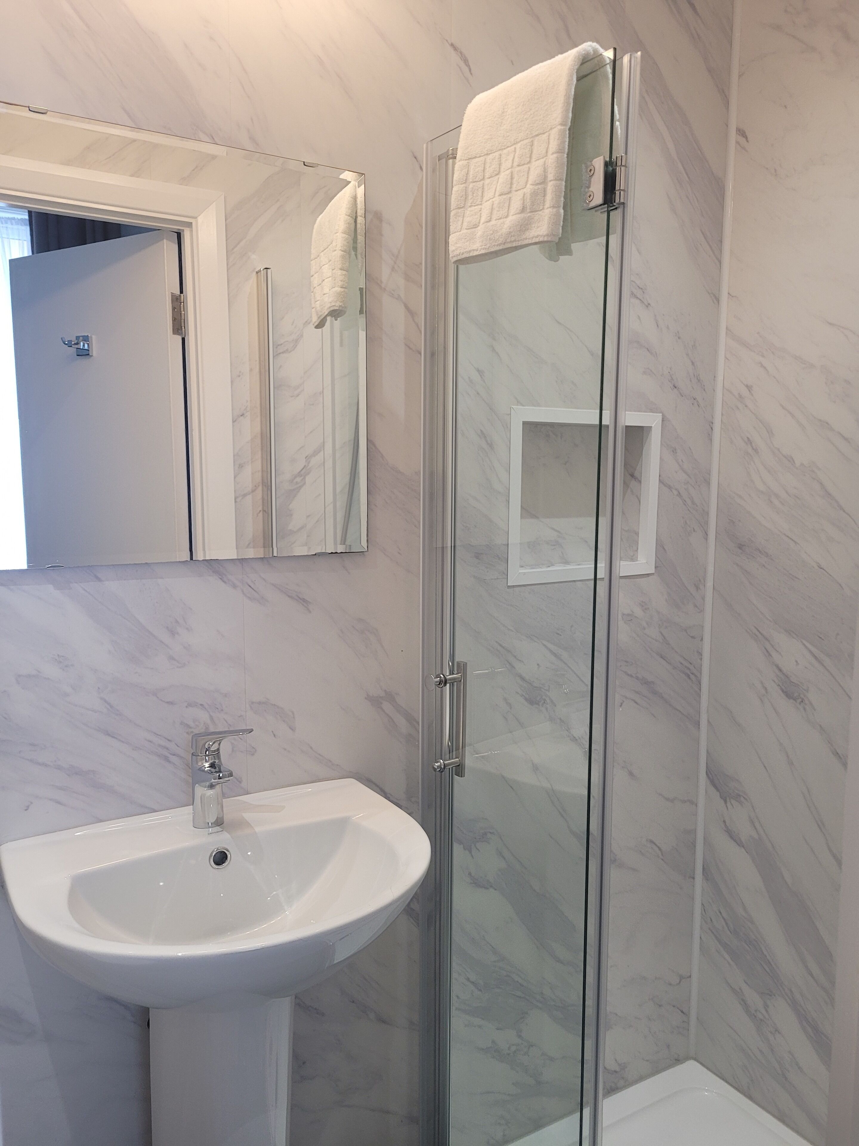 A bathroom with a glass-enclosed shower, a white sink, and a mirror above the sink.