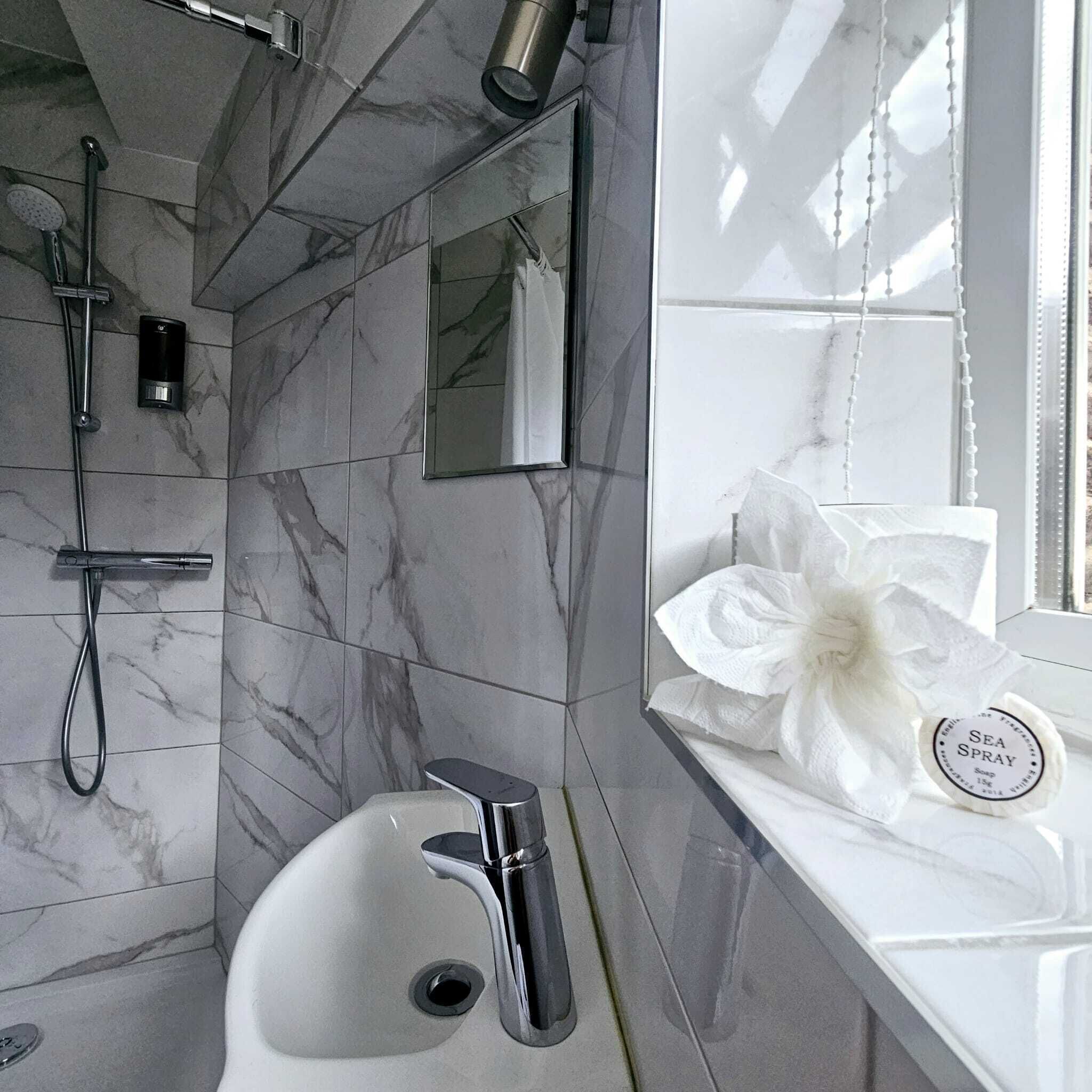 Uma casa de banho moderna com chão de mármore, uma pia, um chuveiro manual e um dispensador de sabonete.
