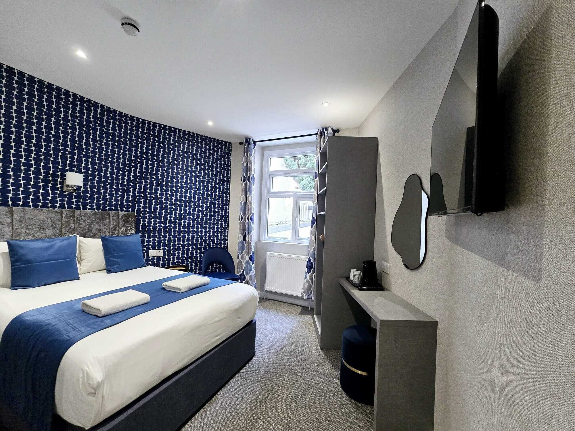 A modern hotel room with a large bed, a built-in TV, and a window with curtains.