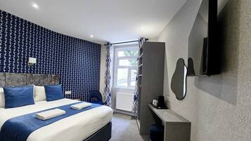 Una habitación de hotel moderna con una cama grande, televisión integrada y ventana con cortinas.