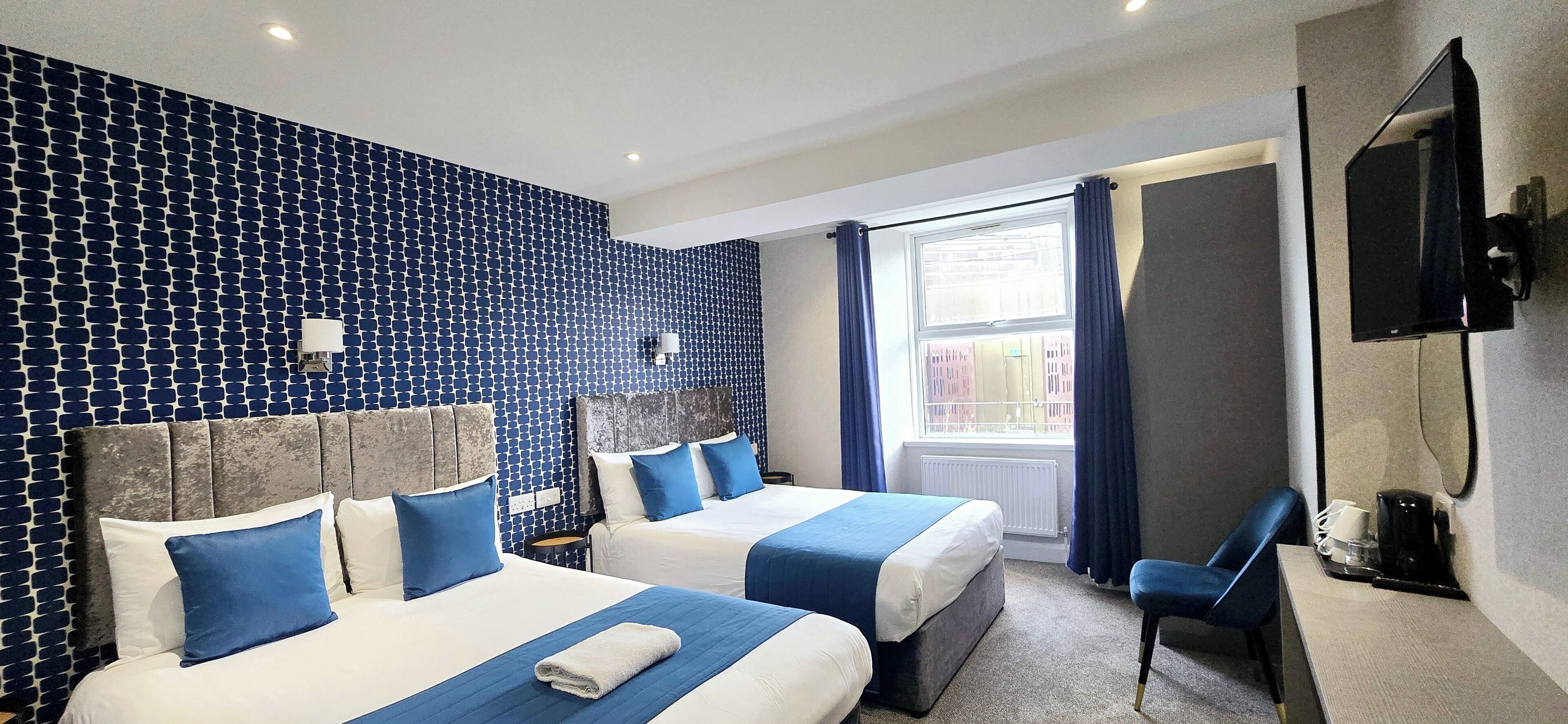 Une chambre d’hôtel avec deux lits, une télévision et une fenêtre avec des rideaux.