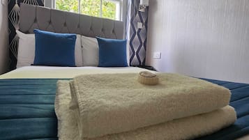 Una cama bien hecha con edredón azul y blanco, una manta blanca esponjosa y una toalla enrollada encima.