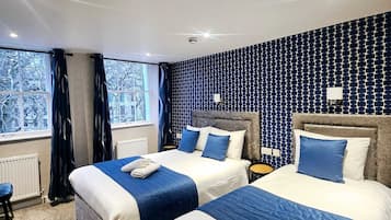 Habitación de hotel con dos camas, un ventanal grande y un papel pintado decorativo.
