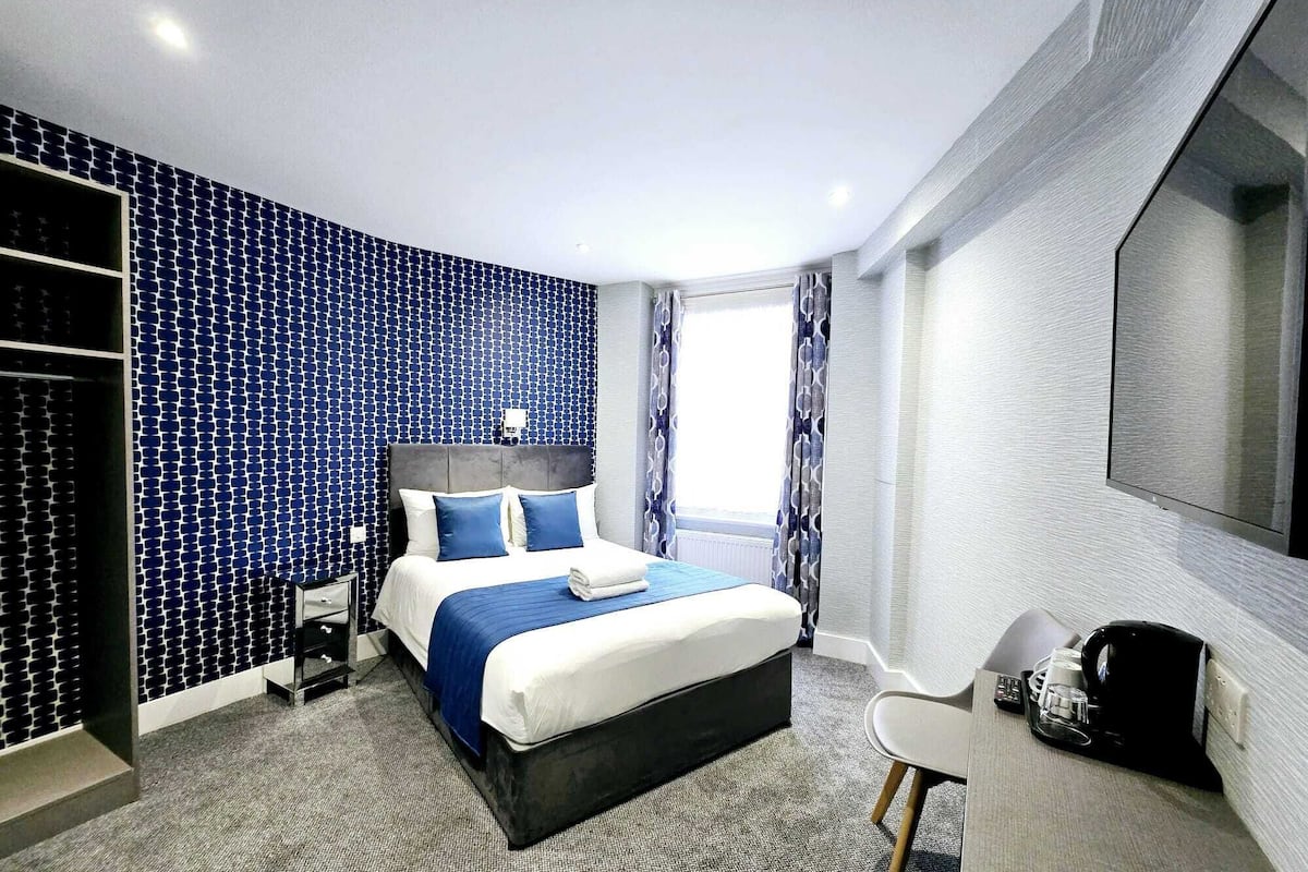 Habitació d'hotel moderna amb un llit gran, un armari, un escriptori amb cadira i un mirall gran.