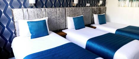 Une chambre d’hôtel avec trois lits, chacun doté de draps blancs et bleus, et un papier peint à motifs.