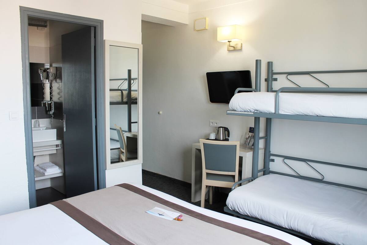 Una habitación de hotel con una litera, un escritorio con una silla, un televisor y un espejo.
