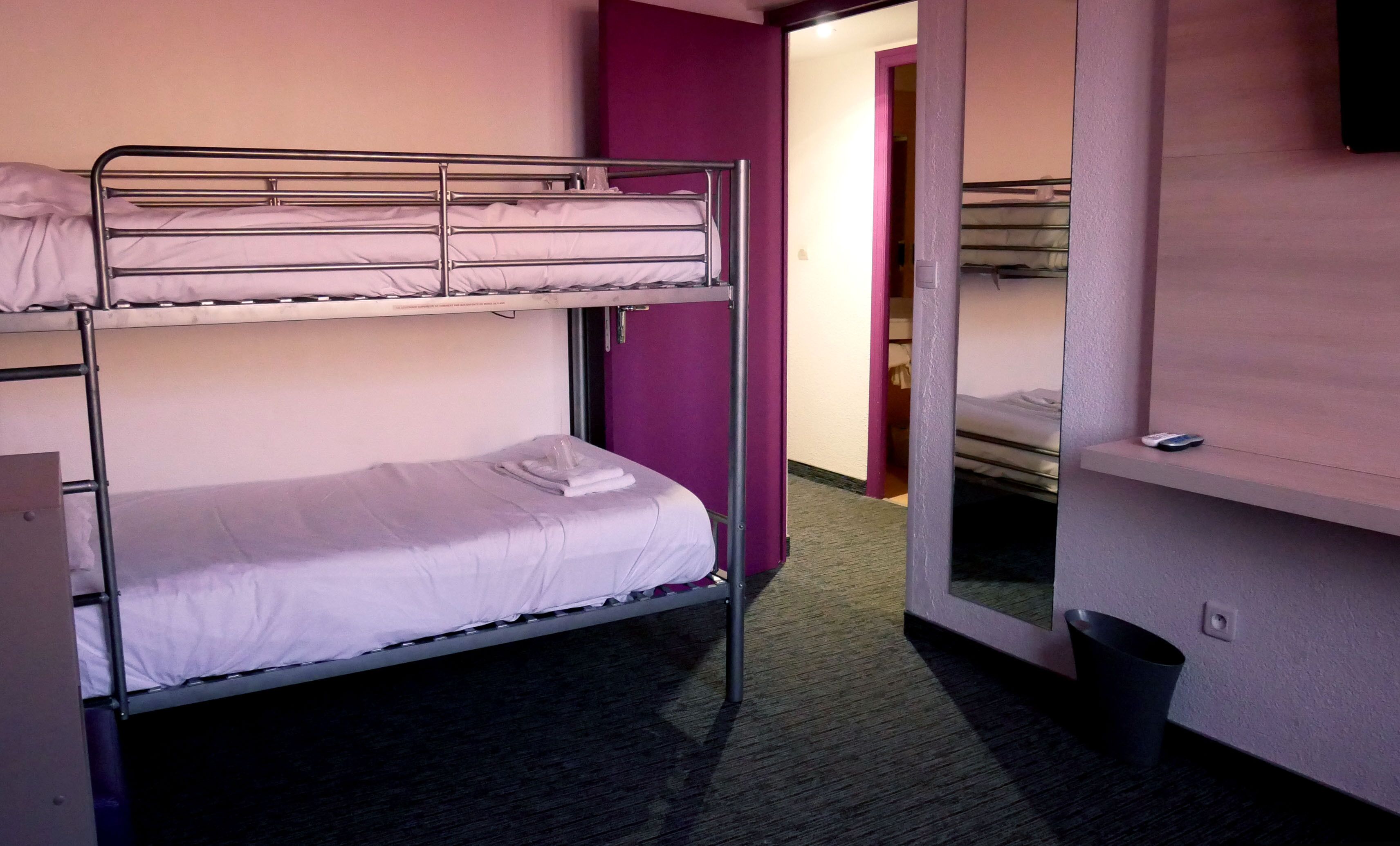 A bunk bed room with a purple wall, a small trash bin, and a remote control on the floor.