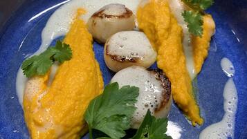 Une assiette en céramique bleue, nappée d’une sauce jaune crémeuse, et garnie de noix de Saint-Jacques et de persil.