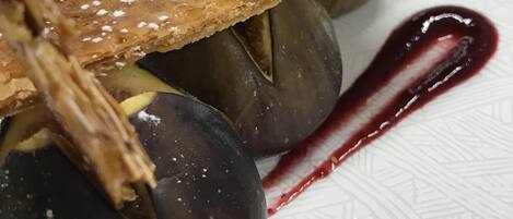 Un plato de postre con una fruta de color oscuro, posiblemente una ciruela, coronado con un hojaldre y espolvoreado con azúcar glas.