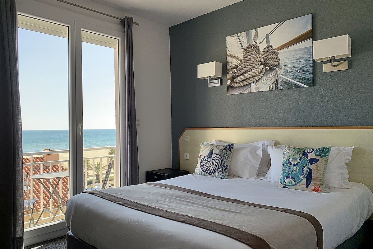 Un cuarto de hotel con una cama grande, vista al mar y un cuadro en la pared.