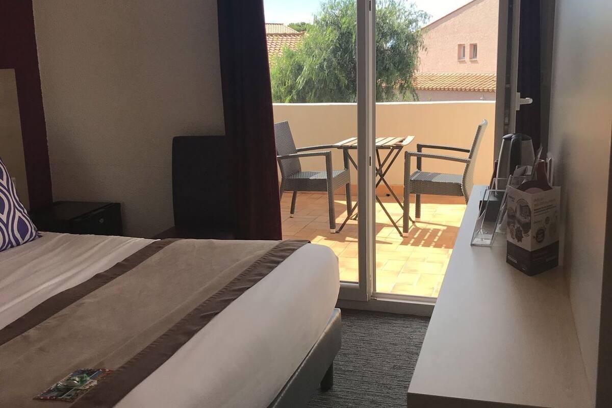 Habitación de hotel con cama, escritorio, silla y vistas al exterior.