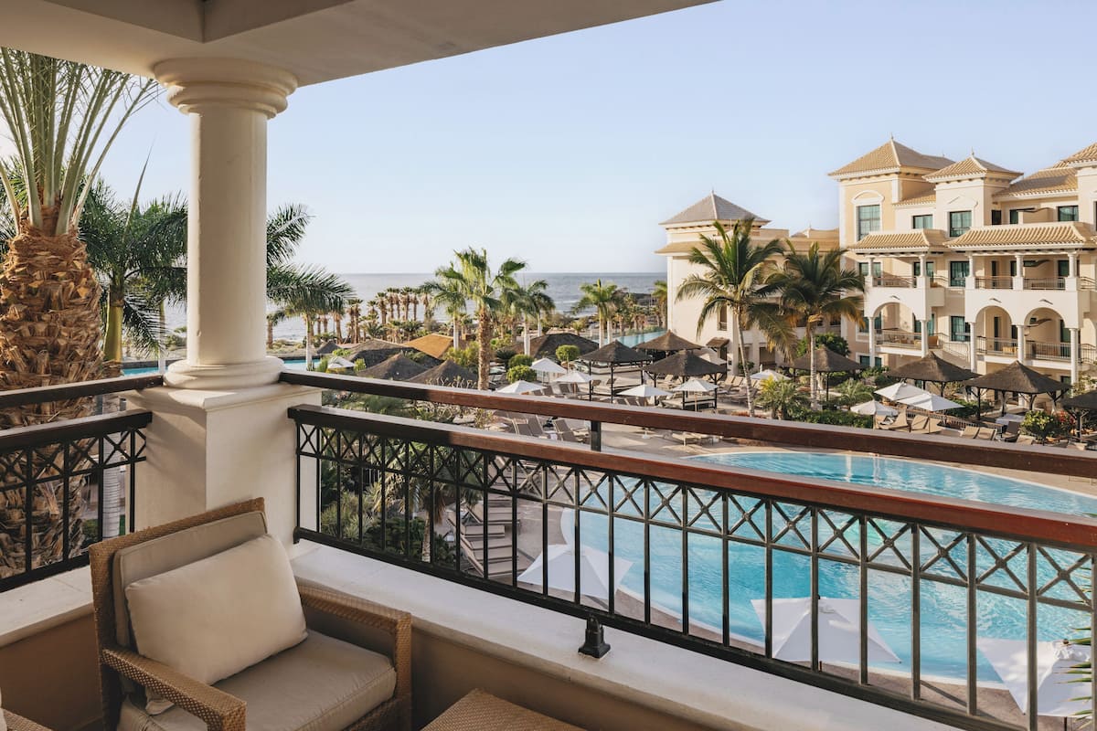 Un balcon d’hôtel avec une piscine, des palmiers et une vue sur l’océan.