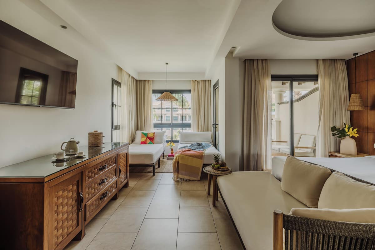 Une chambre d’hôtel moderne dotée d’un grand lit, d’un canapé, d’une table à manger avec une bouilloire et d’un téléviseur fixé au mur.