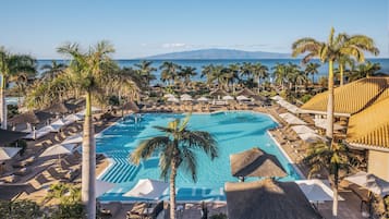 Una piscina de resort con palmeras, sillas de descanso y sombrillas.