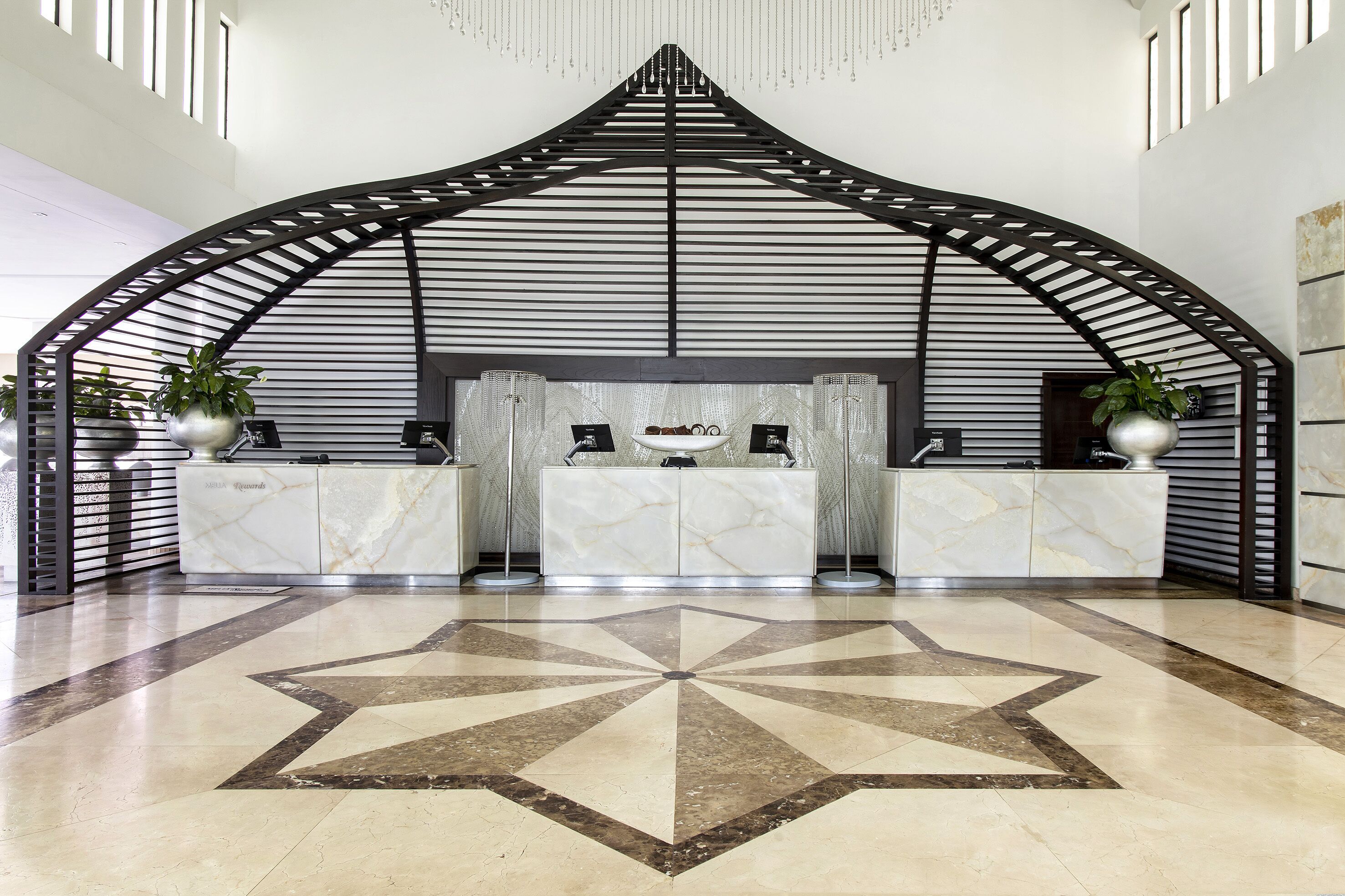 A reception area with a modern design, featuring a marble counter, potted plants, and a geometric floor pattern.