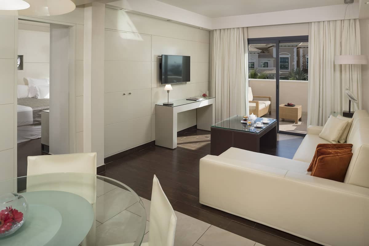 Une chambre d’hôtel moderne avec une table à manger en verre, un canapé, un téléviseur fixé au mur et un balcon avec vue.