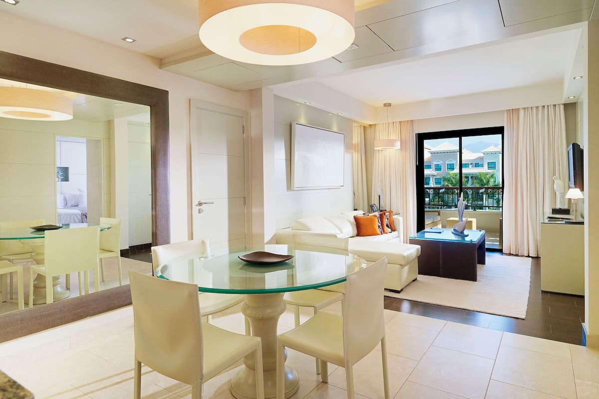 Une chambre d’hôtel moderne dotée d’un coin repas, d’un espace de vie avec un canapé et une table basse, et d’un balcon avec vue.